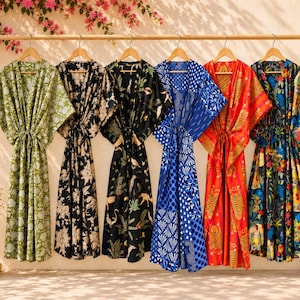 Peut inclure: Six robes caftan longues suspendues sur un portant en bois. Les robes présentent divers motifs, notamment des fleurs vertes, des fleurs noires et crème, une jungle noire, des motifs géométriques bleus, des tigres orange et des fleurs tropicales.