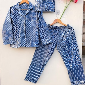 Peut inclure: Un ensemble de pyjama à motifs bleus et blancs, comprenant une chemise boutonnée, un pantalon et une pochette assortie. L'ensemble présente divers motifs géométriques et floraux. Les pyjamas sont suspendus à des cintres en bois.