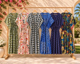 Könnte beinhalten: Sechs Kaftan-Kleider hängen an einem Holzständer. Die Kleider zeigen verschiedene Muster, darunter grüne Kreise, Blumenprints, schwarz-weiße geometrische Designs, blaue Fächermotive, marineblaue Punkte mit rosa Tupfen und ein bunter Tropen-Print.