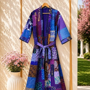 May include: A long-sleeved robe featuring a patchwork design in various shades of purple and blue. The garment is constructed from multiple fabric panels with intricate patterns and is secured at the waist with a matching fabric tie belt.