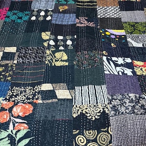 May include: A patchwork quilt featuring a variety of rectangular fabric segments in black, white, teal, orange, and yellow. The textile displays diverse patterns including floral, geometric, striped, and swirling motifs, all joined by visible white running stitches.
