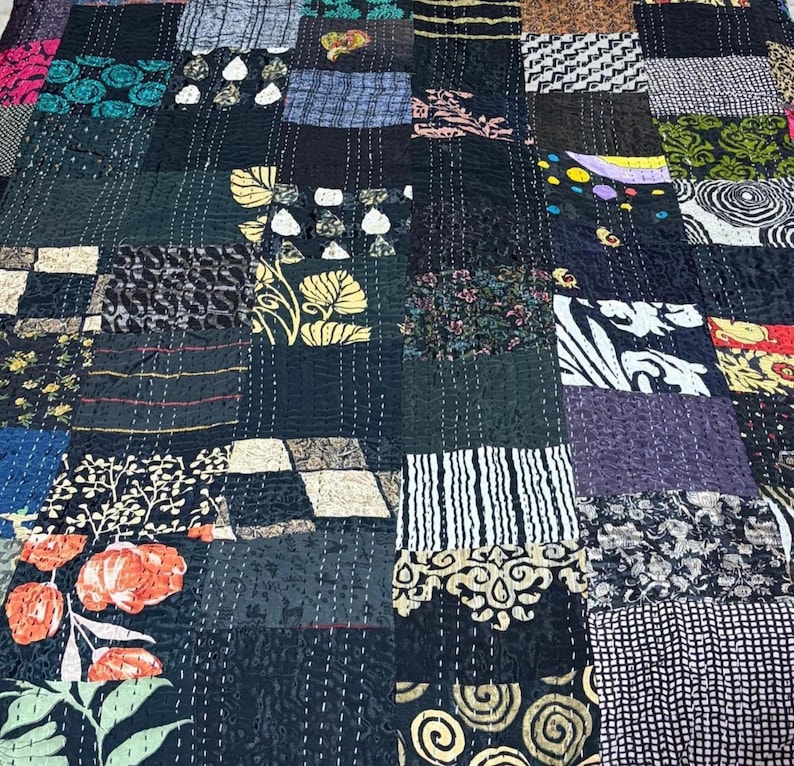 May include: A patchwork quilt featuring a variety of rectangular fabric segments in black, white, teal, orange, and yellow. The textile displays diverse patterns including floral, geometric, striped, and swirling motifs, all joined by visible white running stitches.