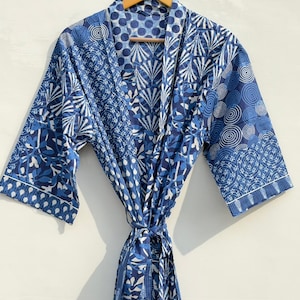 May include: A blue and white patterned robe with a tie closure, hanging on a wooden hanger. The robe features various geometric and floral designs in shades of blue and white. The robe's sleeves are three-quarter length.