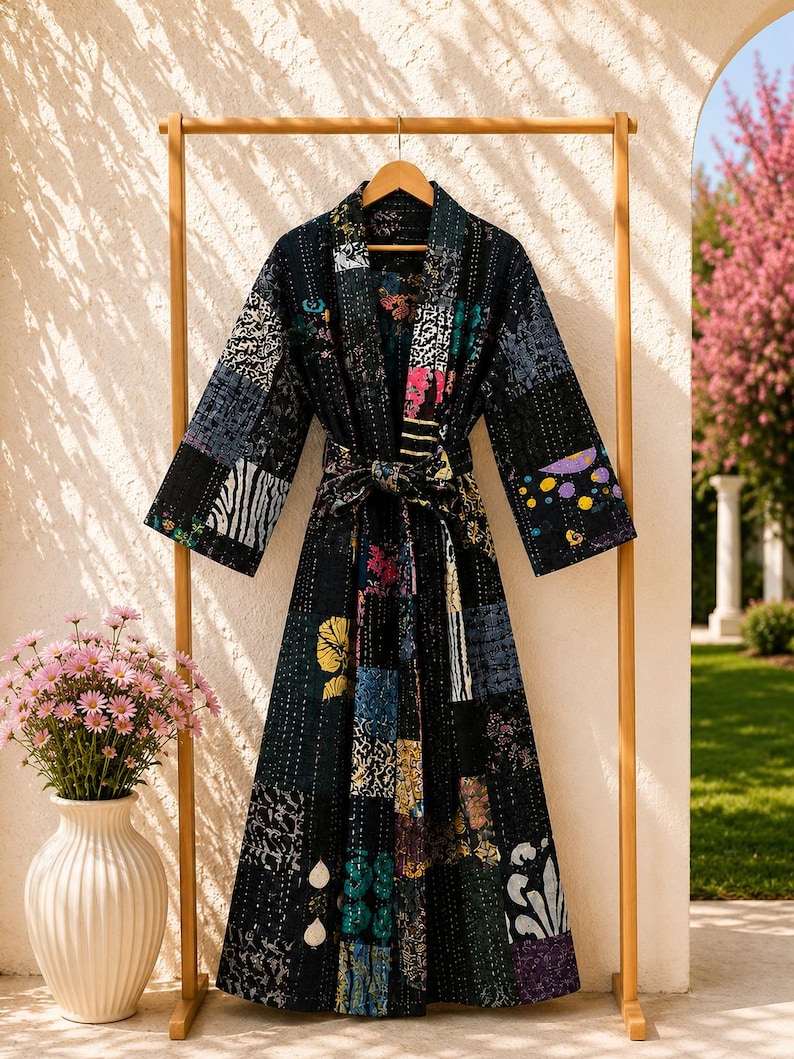 May include: A long-sleeved robe featuring a patchwork design with various dark-toned fabric squares. The garment includes a matching tie belt at the waist, a shawl collar, and visible white stitching throughout the quilted, multi-patterned textile.