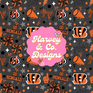 Puede incluir: Un patrón de tela gris oscuro con cabezas de tigre naranjas y negras, megáfonos, pompones, lazos, estrellas y el texto "GO BENGALS" y "B". Una gran etiqueta rosa festoneada en el centro muestra el texto blanco "Harvey & Co. Designs".