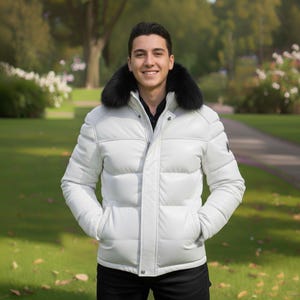 Può includere: Un piumino bianco con collo in pelliccia nera. La giacca presenta un design trapuntato e una chiusura frontale con cerniera. La persona indossa una camicia nera. Lo sfondo è un parco con alberi e vegetazione.