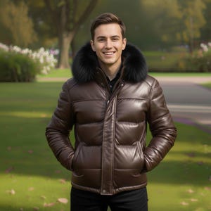 Può includere: Giacca imbottita in pelle marrone con cappuccio foderato in pelliccia nera. La giacca ha una chiusura a zip e tasche. La persona indossa una camicia nera e pantaloni neri. Lo sfondo è un parco con erba verde e alberi.