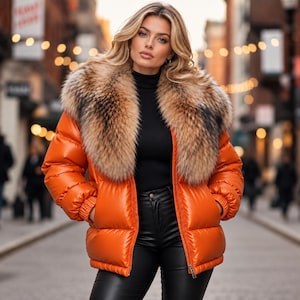 May include: A bright orange puffer jacket featuring a large, thick brown and tan faux fur collar, long sleeves with ribbed cuffs, and a front zipper closure. The jacket is worn over a black turtleneck sweater and black trousers.