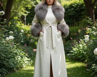 May include: A long, cream-colored coat with a matching belt and a gray fur collar and cuffs. The coat is worn over a white top. The coat is knee-length and has pockets. The background is a garden with white flowers and green grass.