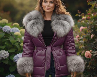 Può includere: Un piumino color prugna con collo e polsini in pelliccia grigia. La giacca ha una cintura abbinata e una chiusura a zip. La modella indossa jeans blu e un top nero. Lo sfondo presenta fiori e vegetazione.
