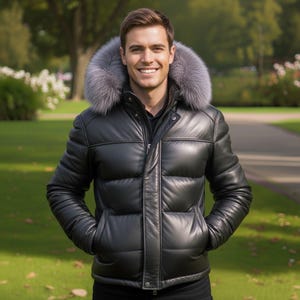 Può includere: Un piumino in pelle nera con cappuccio foderato in pelliccia grigia. La giacca ha una chiusura a zip frontale, tasche e un design trapuntato. La persona indossa la giacca e sorride all'aperto.