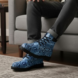 Könnte beinhalten: Ein Paar blaue Stiefel mit Schlangenmuster und schwarzen Schnürsenkeln und Sohlen. Die Stiefel sind hoch und scheinen aus einem strapazierfähigen Material zu sein. Die Stiefel werden mit grauen Jeans getragen.