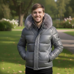 Può includere: Un piumino grigio con cappuccio bordato di pelliccia. La giacca ha una finitura lucida e una chiusura frontale con cerniera. La persona indossa una camicia nera sotto. Lo sfondo è un parco con erba verde e alberi.