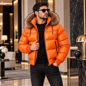 Könnte beinhalten: Eine leuchtend orangefarbene Daunenjacke mit einer großen, braunen Kapuze mit Kunstfellbesatz, einem schwarzen Reißverschluss und gerippten Bündchen. Die Jacke wird über einem schwarzen Langarmshirt und einer dunklen Jeans getragen.