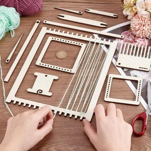May include: A wooden weaving loom kit with various components, including a frame, shuttles, and a comb. The kit is designed for creating woven crafts. The image also shows yarn and a coin.
