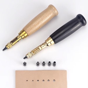 Peut inclure: Deux outils de perforation pour cuir avec des manches en bois et noirs, ainsi que plusieurs têtes de poinçon et un morceau de cuir beige avec des trous perforés. Les outils ont des composants métalliques de couleur laiton.