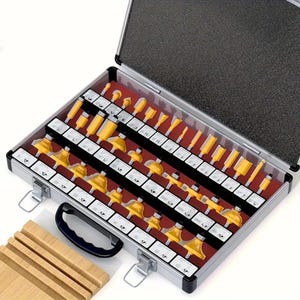 May include: A set of woodworking router bits in a silver metal case. The bits are yellow and arranged in rows on a red felt-lined interior. The case is open, revealing the variety of bit shapes and sizes.