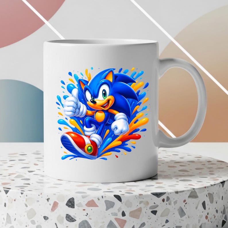 May include: A white ceramic mug featuring a vibrant graphic of the blue character Sonic giving a thumbs up. The design includes dynamic splashes of blue, yellow, and orange paint surrounding the character, who wears white gloves and red shoes.