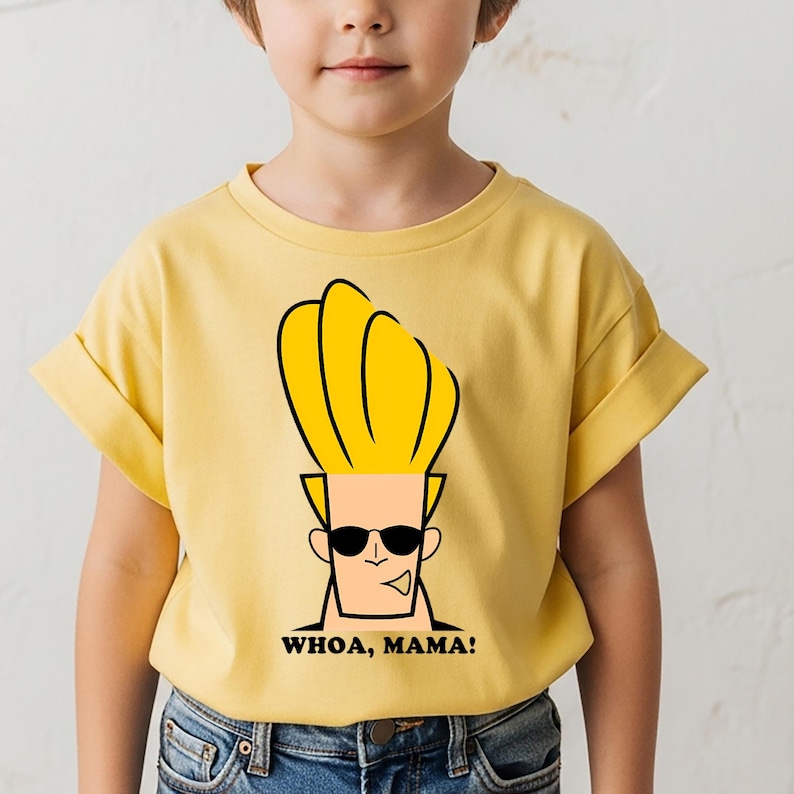 May include: A light yellow short-sleeved t-shirt featuring a graphic print of the cartoon character Johnny Bravo with his signature tall blonde hair and black sunglasses. Below the character, the text reads WHOA, MAMA! in bold black letters.