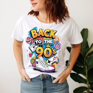 May include: A white short-sleeved t-shirt featuring a colourful graphic print with the text BACK TO THE 90'S. The design includes a cassette tape, a game controller, a high-top sneaker, and lollipops, all rendered in vibrant yellow, blue, and purple.