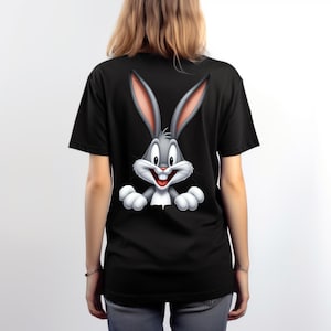 May include: A black short-sleeved t-shirt featuring a large, centred graphic of the cartoon character Bugs Bunny. The character is depicted with long grey ears, a white muzzle, and white paws, appearing as if peeking over the bottom of the design.