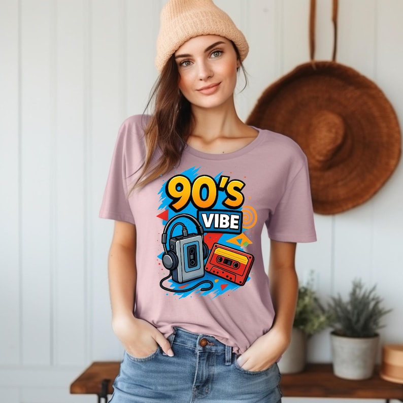 May include: A light mauve t-shirt featuring a graphic print with the text 90's VIBE in yellow and blue, accompanied by illustrations of a grey portable cassette player with black headphones and a red and yellow cassette tape on a blue background.