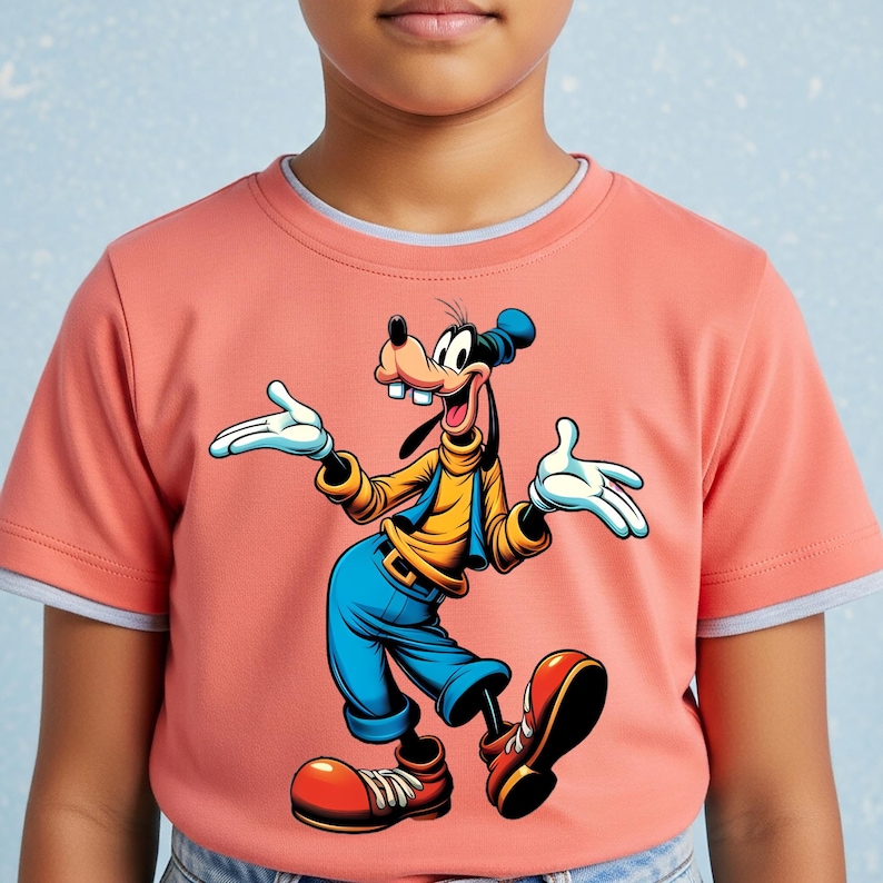 May include: A coral-coloured short-sleeved t-shirt featuring a graphic print of the cartoon character Goofy. The character is depicted with a yellow turtleneck, blue vest, blue pants, and large red shoes, standing with arms outstretched.