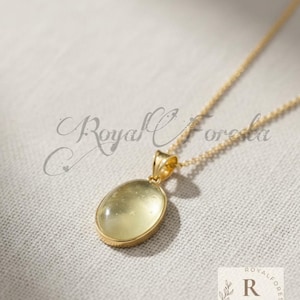 Puede incluir: Un collar dorado con un colgante ovalado de piedra preciosa verde claro. El colgante está engastado en un bisel dorado y cuelga de una fina cadena dorada. La imagen tiene el texto "Royal Foresta" y un logotipo en la esquina inferior derecha.