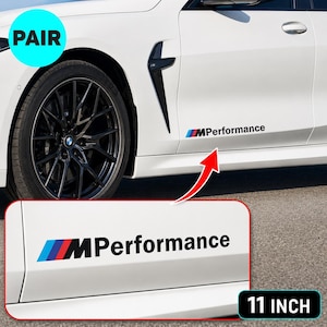 Op de afbeelding: Een paar zwarte en meerkleurige MPerformance vinylstickers voor het zijpaneel van een auto. De tekst luidt MPerformance met een blauw, paars en rood logo. De sticker is 27,94 cm lang, zoals getoond in de productafbeelding op een witte auto.