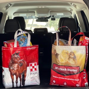 May include: Two large feed bags in a car trunk. One red bag features a brown horse and the Purina logo. The other bag is red and white, with an image of chicks and the text "18% Chick Starter".