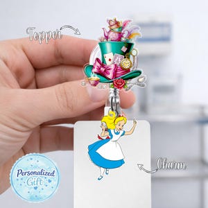 May include: A badge reel with an Alice in Wonderland theme. The topper features a green top hat with a pink bow, playing cards, and a teapot. The charm shows Alice in a blue dress. The text "Personalized Gift" is on a blue circle.