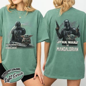 May include: Light green t-shirts featuring Star Wars: The Mandalorian graphics. The front of the shirt displays the Mandalorian and Grogu, while the back shows the Mandalorian holding blasters with Grogu. The text "STAR WARS THE MANDALORIAN" is printed on both sides.