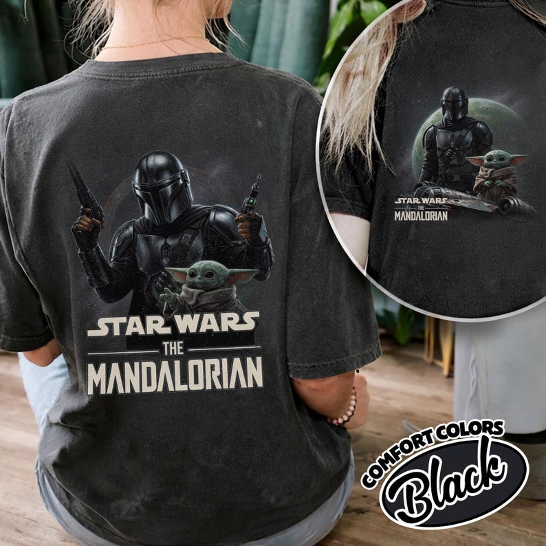 May include: Black t-shirt featuring a graphic of The Mandalorian and Grogu from Star Wars. The Mandalorian is depicted in armor, holding blasters, with Grogu below. The text "STAR WARS THE MANDALORIAN" is printed in white.