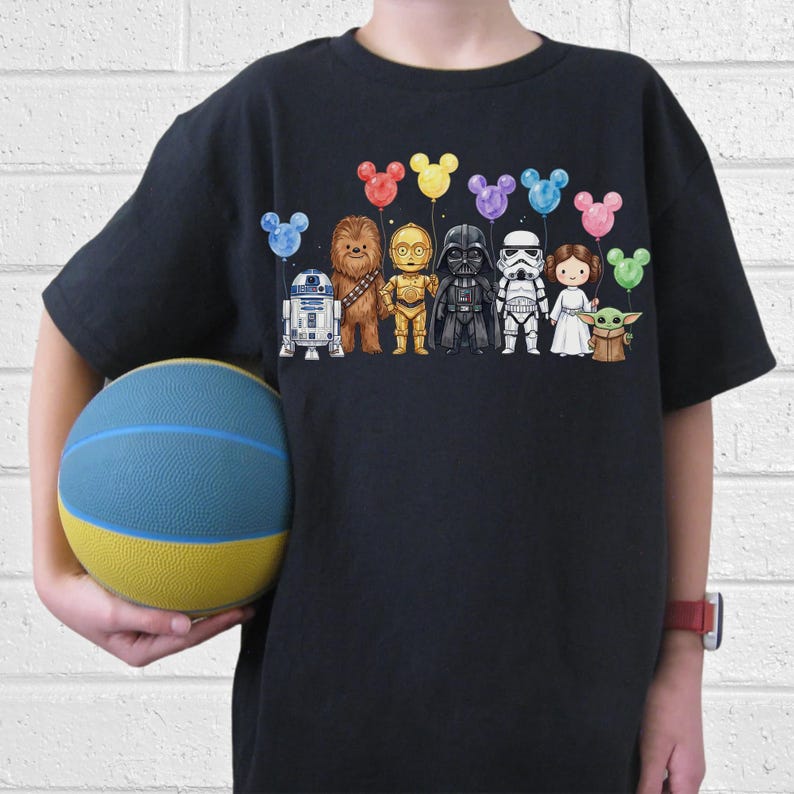 Op de afbeelding: Zwart T-shirt met een Star Wars-ontwerp. De afbeelding toont cartoonversies van personages als R2-D2, Chewbacca, C-3PO, Darth Vader, een Stormtrooper, Princess Leia en Baby Yoda, elk met een Mickey Mouse-vormige ballon.