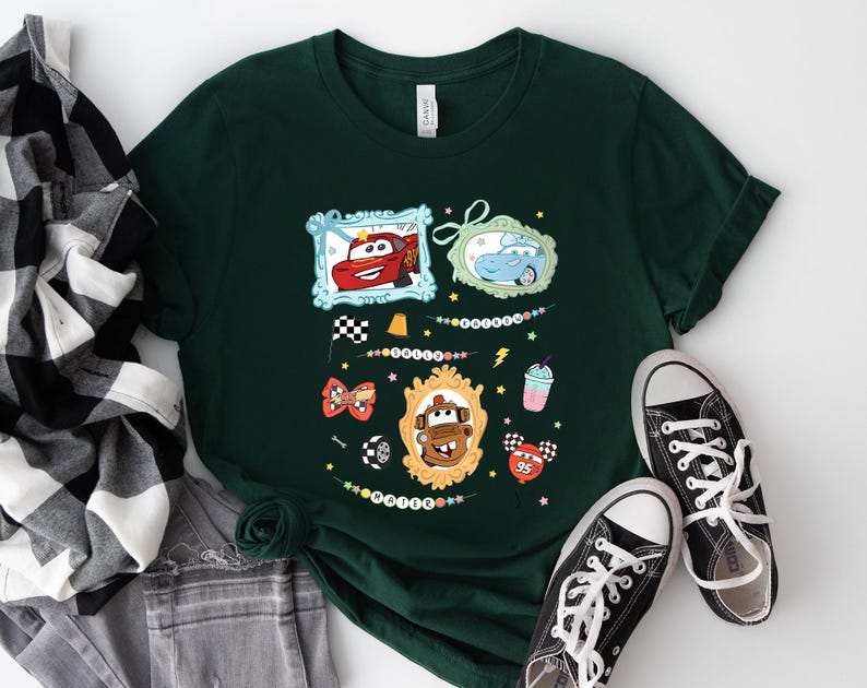 Puede incluir: Camiseta verde oscuro con personajes de dibujos animados de coches en marcos ornamentados. La camiseta incluye una bandera a cuadros, una pajarita y un gr&aacute;fico de batido. Zapatillas de lona negras con cordones blancos junto a la camiseta.