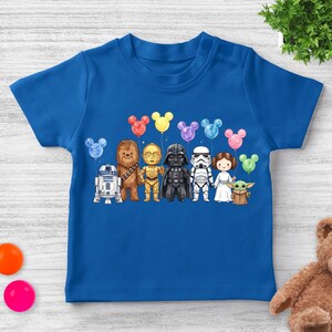 Op de afbeelding: Een blauw T-shirt met een aquarel illustratie van Star Wars-personages die Mickey Mouse-vormige ballonnen vasthouden. De personages zijn R2-D2, Chewbacca, C-3PO, Darth Vader, een Stormtrooper, Princess Leia en Grogu.