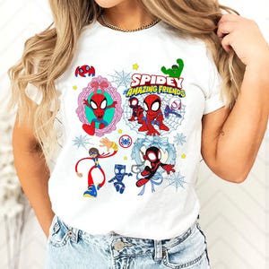May include: White t-shirt featuring a colorful graphic of Spider-Man and friends. The design includes the text "Spidey and His Amazing Friends" with various cartoon characters and spiderwebs. The shirt is worn by a person.