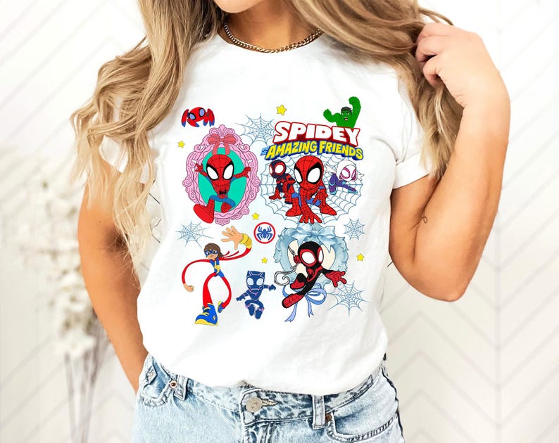 May include: White t-shirt featuring a colorful graphic of Spider-Man and friends. The design includes the text "Spidey and His Amazing Friends" with various cartoon characters and spiderwebs. The shirt is worn by a person.