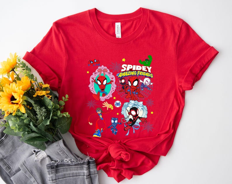 May include: Red t-shirt featuring a colorful graphic of Spidey and his Amazing Friends. The design includes various characters and the text "Spidey and Amazing Friends". The shirt is made of a soft material.