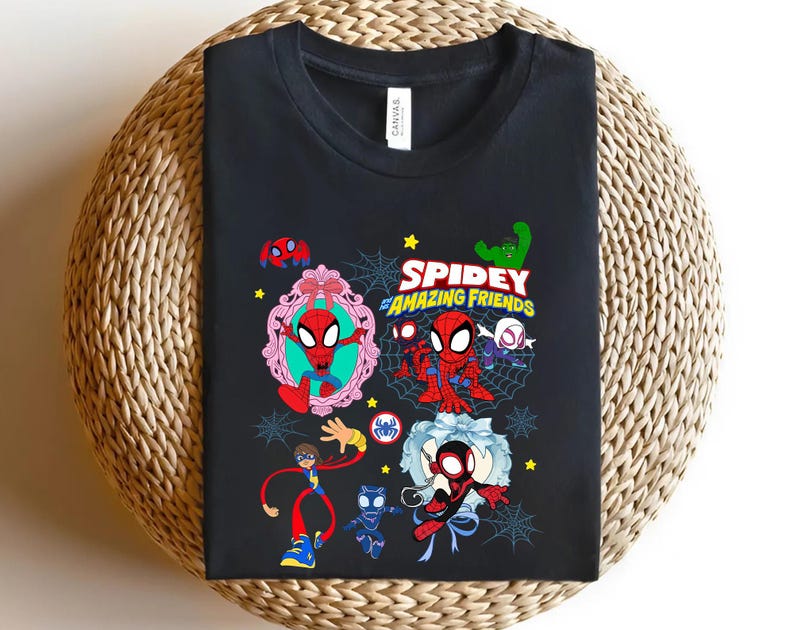 May include: Black t-shirt featuring a colorful graphic of Spider-Man and his friends. The design includes the text "Spidey and Amazing Friends" with various cartoon characters and web designs. The shirt is displayed on a woven surface.