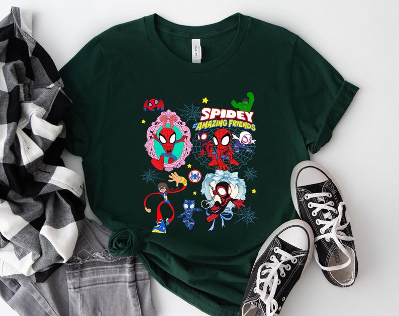 May include: Dark green t-shirt featuring a colorful graphic of Spider-Man and friends with the text "Spidey and His Amazing Friends". The design includes various characters and spiderwebs. Black canvas sneakers with white laces are next to the shirt.