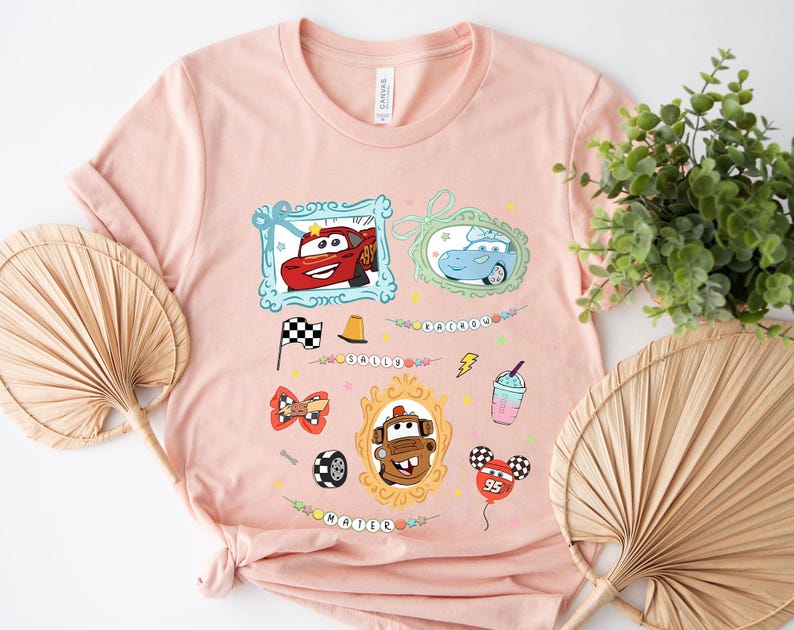 Puede incluir: Una camiseta rosa claro con im&aacute;genes de dibujos animados de personajes de la pel&iacute;cula Cars. El dise&ntilde;o incluye im&aacute;genes enmarcadas de Rayo McQueen, Sally y Mate, junto con otros gr&aacute;ficos tem&aacute;ticos y los nombres "Sally" y "Mater".