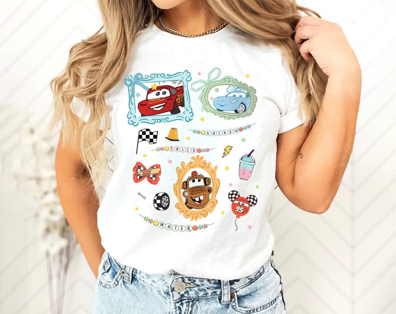Puede incluir: Camiseta blanca con im&aacute;genes de dibujos animados de personajes de Cars, incluyendo a Rayo McQueen y Mate, en marcos decorativos. Otros gr&aacute;ficos incluyen una bandera a cuadros, un cono de tr&aacute;fico y un globo.
