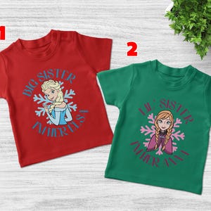 May include: Two short-sleeved t-shirts, one red and one green. The red shirt features a graphic of Elsa with the text "Big Sister" and "Father Elsa". The green shirt has a graphic of Anna with the text "Lil' Sister" and "Father Anna".
