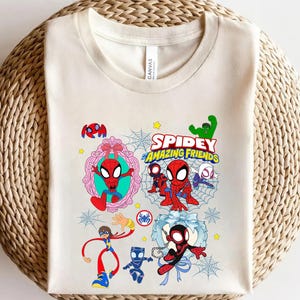 May include: Cream-colored t-shirt featuring a colorful graphic of Spider-Man and friends. The design includes the text "Spidey and His Amazing Friends" with cartoon illustrations of the characters, spider webs, and stars.