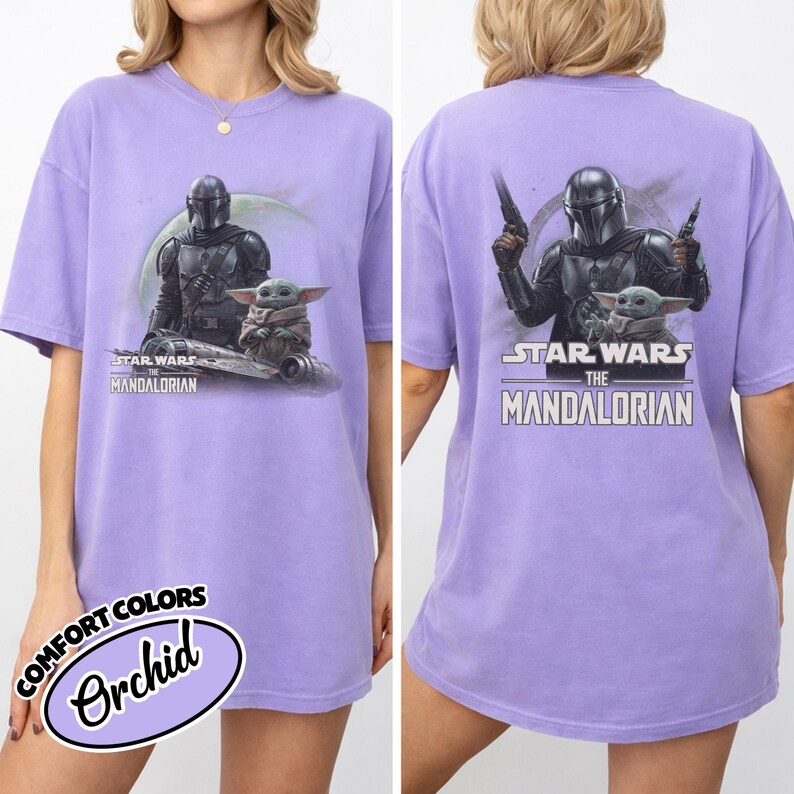 May include: Orchid-colored t-shirt featuring a graphic of The Mandalorian and Grogu from Star Wars. The front shows the characters with the text "STAR WARS THE MANDALORIAN". The back of the shirt also displays the characters and text. The shirt is a Comfort Colors brand.