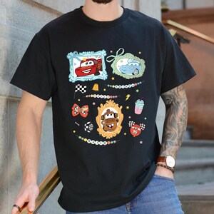 Puede incluir: Camiseta negra con gr&aacute;ficos de coches de dibujos animados coloridos en marcos ornamentados. El dise&ntilde;o incluye im&aacute;genes de Rayo McQueen, Mate y otros personajes de la pel&iacute;cula Cars, junto con elementos decorativos como una bandera a cuadros y un batido.