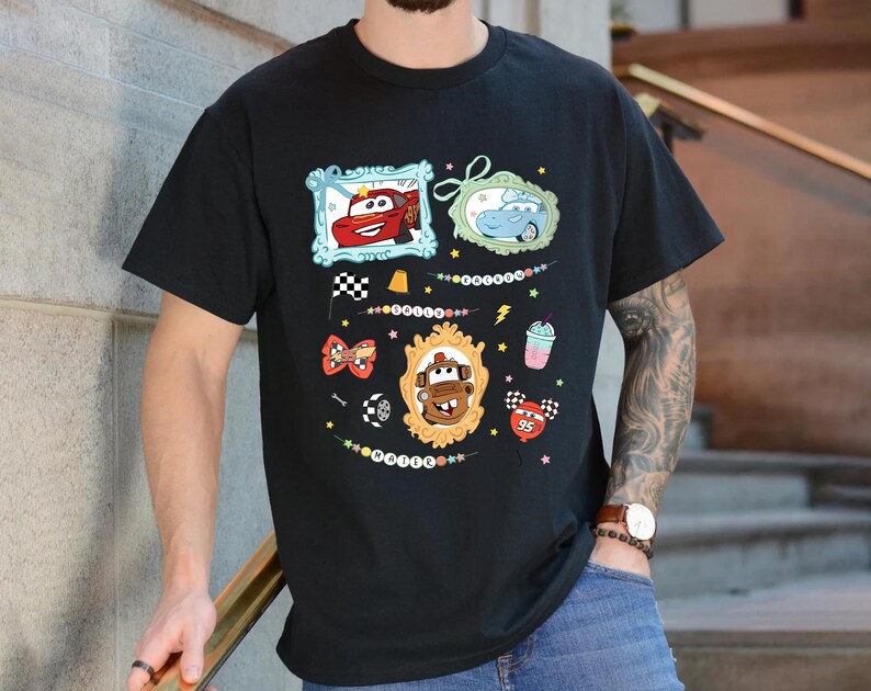 Puede incluir: Camiseta negra con gr&aacute;ficos de coches de dibujos animados coloridos en marcos ornamentados. El dise&ntilde;o incluye im&aacute;genes de Rayo McQueen, Mate y otros personajes de la pel&iacute;cula Cars, junto con elementos decorativos como una bandera a cuadros y un batido.