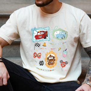 Puede incluir: Camiseta color crema con im&aacute;genes de dibujos animados de los personajes de la pel&iacute;cula Cars. El dise&ntilde;o incluye im&aacute;genes enmarcadas de Rayo McQueen y Mate, junto con otros gr&aacute;ficos relacionados como una bandera a cuadros y un globo.