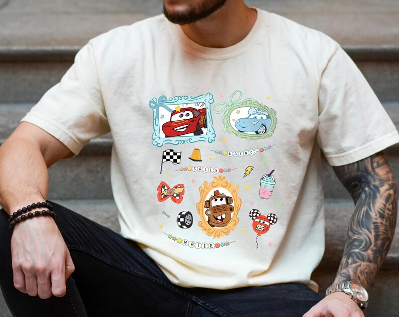 Puede incluir: Camiseta color crema con im&aacute;genes de dibujos animados de los personajes de la pel&iacute;cula Cars. El dise&ntilde;o incluye im&aacute;genes enmarcadas de Rayo McQueen y Mate, junto con otros gr&aacute;ficos relacionados como una bandera a cuadros y un globo.